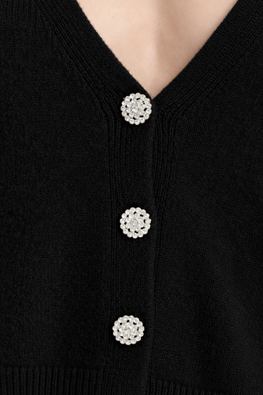 a woman wearing a black cardigan with detailed shiny buttons