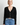 A woman wearing a black cardigan and blue jeans on a white background.