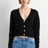 A woman wearing a black cardigan and blue jeans on a white background.