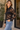 a woman wearing a lace sheer blouse with a bralette and blue jeans in outside a house setting.