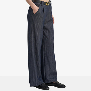 A person wearing dark navy pinstriped wide-leg trousers with a black belt and black loafers, shown from the waist down against a light gray studio background.