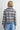 A woman facing backwards in a blue plaid flannel jacket and blue jeans on a white background.