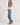 A woman wearing a cream knit sweater with a brown and burgundy geometric pattern across the chest and green ribbed cuffs and hem, paired with blue jeans On white background