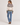 A woman wearing a cream knit sweater with a brown and burgundy geometric pattern across the chest and green ribbed cuffs and hem, paired with blue jeans on white background