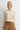 A woman wearing an embellished cream knit sweater and mustard yellow pants on a white background.