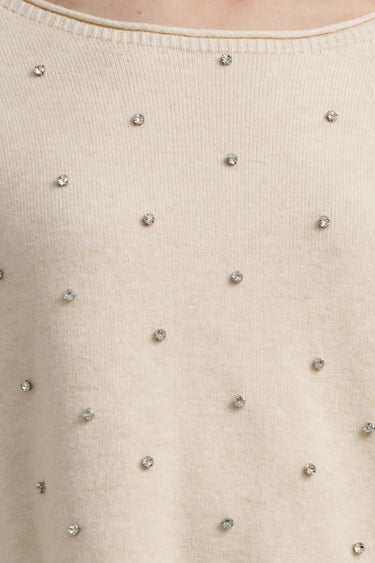 A close up of a cream colored embellished knit sweater.