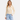 A woman wearing a sheer lace blouse in cream and black jeans on a white background.
