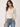 A woman wearing a sheer lace blouse in cream and black jeans on a white background.