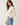 A woman wearing wearing a sheer lace blouse in cream and black jeans on a white background.