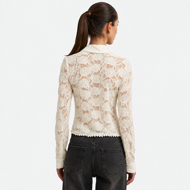 a woman facing backward wearing a sheer lace blouse in cream and black jeans on a white background.