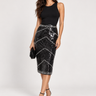 A woman wearing a black tank top and a silver studded black sequin midi skirt with black open  heels on a studio background