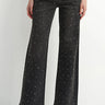 A model wearing black embellished wide leg jeans and black heeled boots on a white background.