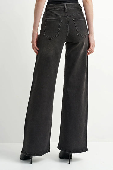 A model wearing black wide leg jeans and black heeled boots on a white background.
