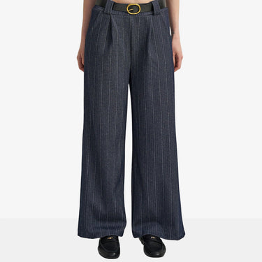 A model is shown from the waist down wearing high-waisted, wide-leg trousers in a dark navy blue with fine vertical white pinstripes. The pants are styled with a black leather belt featuring a gold oval buckle and black leather loafers, set against a plain light gray studio background.