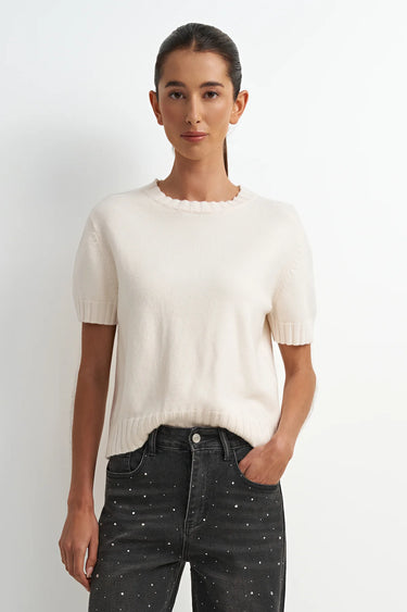 Woman wearing a white knit top and black pants against a white background