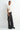 Woman wearing a white top and black pants with a small black handbag on a white background