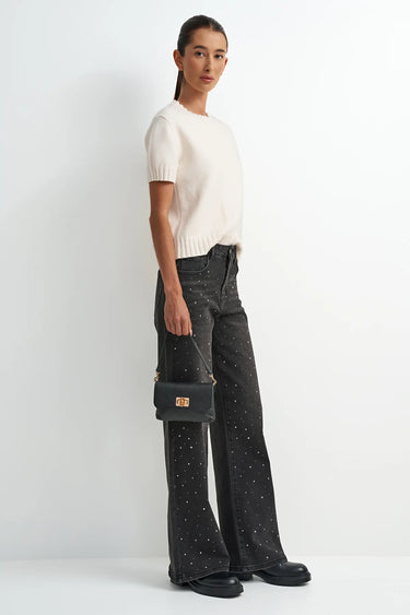 Woman wearing a white top and black pants with a small black handbag on a white background