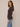 A woman modeling a dark brown ribbed cardigan with front buttons, paired with light blue jeans, against a plain beige studio background.