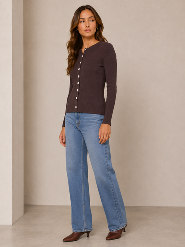 A woman modeling a dark brown long-sleeve button-front cardigan with light-wash blue jeans and brown pointed-toe heels, standing against a neutral beige studio wall.