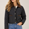 A woman wearing a black diamond-quilted jacket with a brown collar and pocket trim, paired with blue jeans, against a light beige studio background.