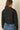 a woman wearing a black quilted jacket with a brown corduroy collar on a neutral background.