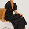 woman wearing black embroidery blouse and skirt seated on a chair on white background