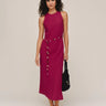 Woman wearing a sleeveless magenta dress with buttons on a plain background