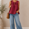 Woman wearing a red sleeveless top and blue jeans standing indoors.