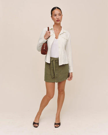 Woman wearing a white shirt, green skirt, and black shoes on a beige background