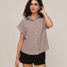 Woman wearing a checkered shirt and black shorts against a beige background