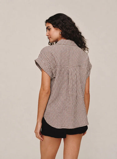 Woman wearing a brown gingham shirt and black shorts on a plain background