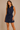 Woman wearing a navy sleeveless dress with buttons on a beige background