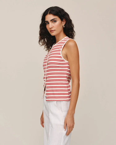 Woman wearing a red and white striped sleeveless top with white pants on a beige background