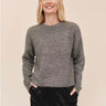 A woman wearing A slouchy metallic crewneck sweater with black jeans on a studio background.