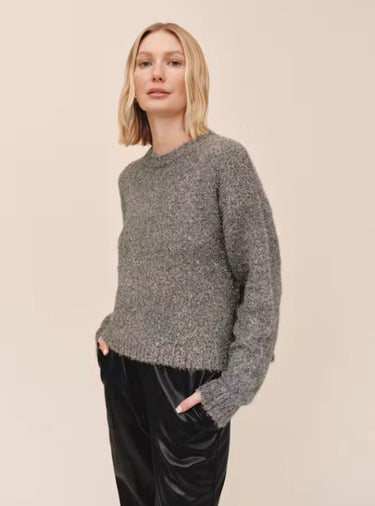 A  woman wearing a slouchy metallic crewneck sweater with black jeans on a studio background.