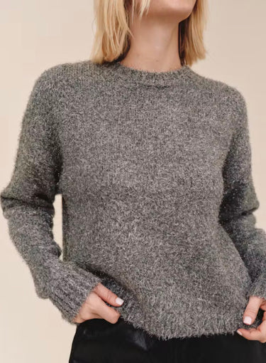A slouchy metallic crewneck sweater with black jeans on a studio background.