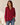 A woman wearing a long-sleeve button-up shirt in deep burgundy with two chest pockets, paired with blue jeans, standing against a warm beige background.
