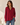 A woman wearing a long-sleeve button-up shirt in deep burgundy with two chest pockets, paired with blue jeans, standing against a warm beige background.