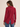 A woman shown from the back wearing a long-sleeve red button-up shirt with a curved hem and blue jeans, set against a plain beige studio background.