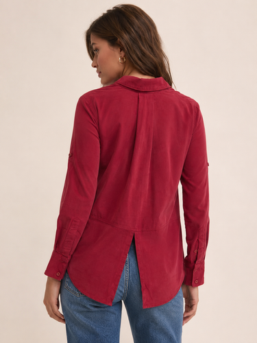 A woman shown from the back wearing a long-sleeve red button-up shirt with a curved hem and blue jeans, set against a plain beige studio background.