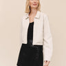 A woman wearing a black top, leather skirt, and a cropped blazer on a white background.