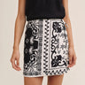 Person wearing a black and white patterned skirt with a plain background