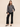 A woman wearing a smoke grey striped blouse and black jeans on a studio background.