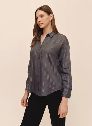 A woman wearing a smoke grey striped blouse and black jeans on a studio background.