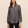 A woman wearing a smoke grey striped blouse and black jeans on a studio background.