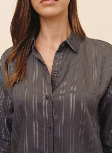 A close up of a woman wearing a stripe button down on a studio background.