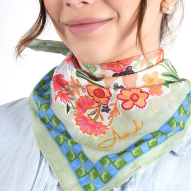 Woman wearing a colorful green floral scarf with a brand logo on a white background