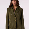 A woman models an olive green blazer, paired with wide-leg blue jeans against a plain light background.