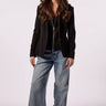A woman modeling a black blazer over a black top with wide-leg blue jeans, standing against a light gray studio background.