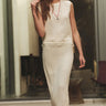 A woman wearing a cream colored cotton mesh vest with fringe detail and a matching maxi skirt with fringe detail at the bottom